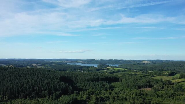 Wide aerial view of Lac des Settons surrounded by lush forests and rolling hills under a blue sky. Scenic natural landscape in Burgundy, France.