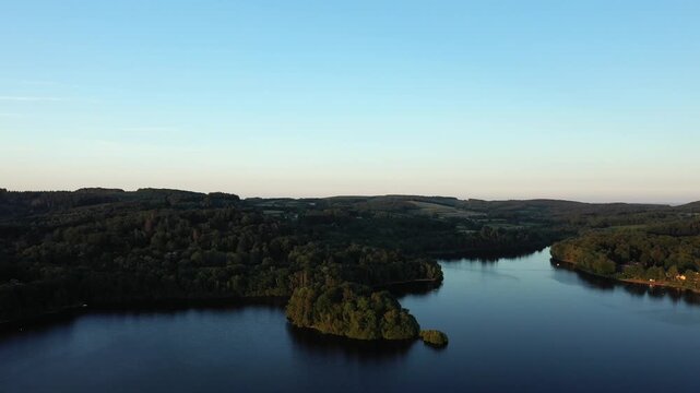 Scenic aerial landscape of Lac des Settons surrounded by lush forest and calm water under a clear evening sky in Burgundy, France.