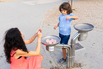 Fototapeta premium Mother and son filling water balloons at fountain
