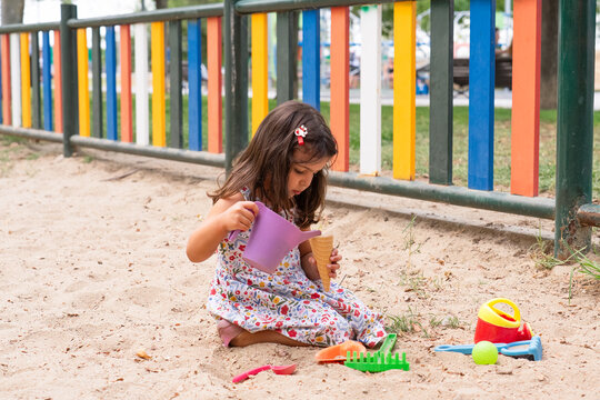 Little girl playing with colorful toys in sandbox