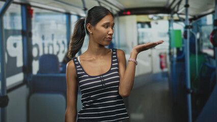 Fototapeta premium Thai woman holding palm up inside bus on street, wearing striped tanktop and bracelet; resignation patience.