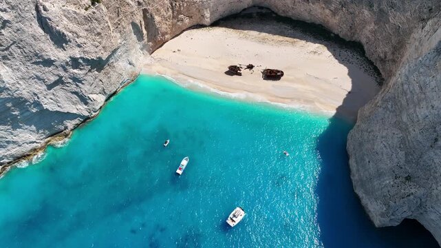 Aerial drone view of famous Navagio Shipwreck Beach with turquoise sea water and boats in Zakynthos island, Greece on a bright sunny da