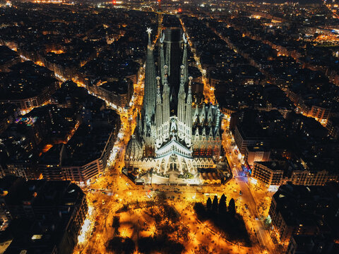 Aerial view of the illuminated Sagrada Familia cathedral piercing the dark cityscape, a beacon of light amidst the urban night, Barcelona, Catalonia, Spain.