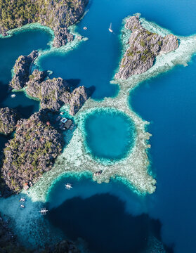 Aerial view of the vibrant turquoise lagoon ringed by jagged limestone cliffs and coral reefs, a tropical jewel amidst the azure sea, Coron, Mimaropa, Philippines.