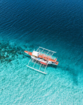 Aerial view of a vibrant outrigger boat floating on the turquoise waters, a dance of light and shadow creating a mesmerizing scene, Coron, Mimaropa, Philippines.