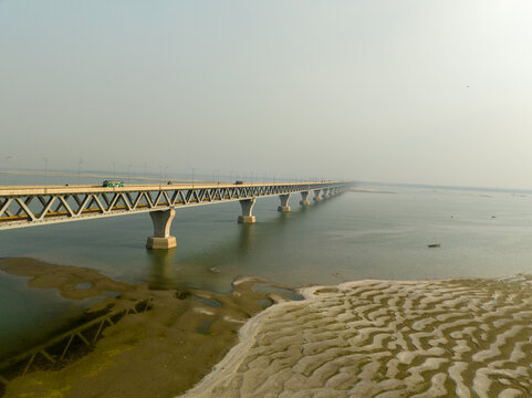 Aerial view of the Padma Multipurpose Bridge stretches across the tranquil waters, connecting shores under a hazy sky, Mawa, Dhaka Division, Bangladesh.