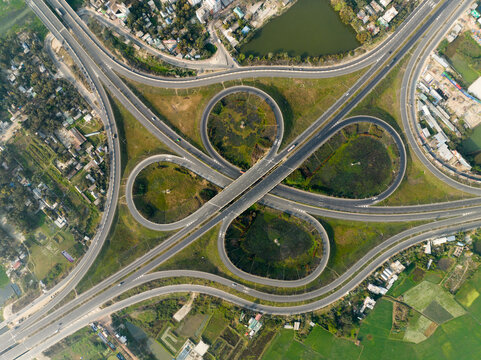 Aerial view of intricate cloverleaf interchange weaving through the landscape, showcasing engineering amidst verdant fields, Bhanga, Dhaka Division, Bangladesh.