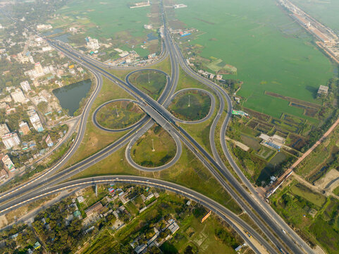 Aerial view of a cloverleaf interchange with smooth curves and symmetrical loops amidst the sprawling green landscape, Bhanga, Dhaka Division, Bangladesh.