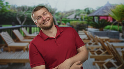 Fototapeta premium Man laughing and holding stomach in red polo on street deck with lounge chairs; vacation joy relaxation.