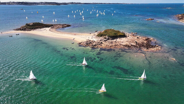 Aerial view of sailboats gliding across the turquoise waters around the rocky Ile Callot, a captivating dance of white sails against the Brittany coastline, Carantec, Brittany, France.