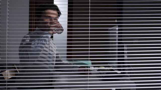 Office worker at computer clutching pills and a glass of water, showing fatigue and stress from overwork in a modern corporate desk environment, seeking relief from headache