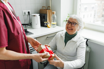 Unrecognizable social worker volunteer greeting her old lonely patient in wheelchair with...