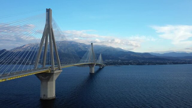 Wide view of the Rion Antirion Bridge spanning across blue water with mountains in the background, under a clear sky in Greece.