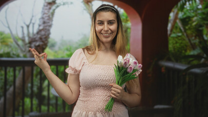 Naklejka premium Woman holding pink tulip bouquet with left hand, right hand forming ok sign near shoulder, eyes closed on a covered building balcony with railing; serenity.
