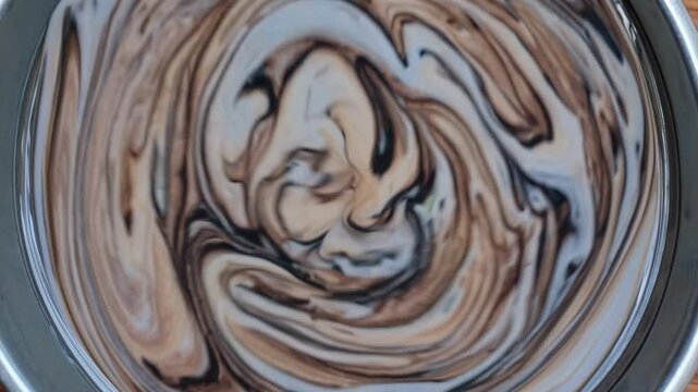 Swirling mixture of cream and chocolate in a metal bowl, showcasing the gradual blending of colors and textures in a visually appealing culinary process