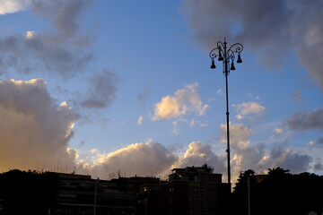 Silhouetted street lamp against dramatic evening sky over urban buildings