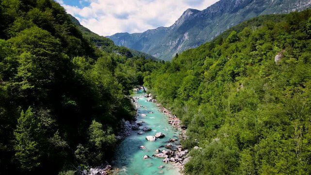 Aerial view of the bright turquoise Soca River snaking through a lush green valley, surrounded by steep mountains, Kobarid, Tolmin, Slovenia.