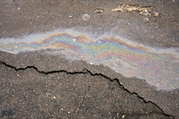 Iridescent oil slick spreading on damaged asphalt surface, reflecting vibrant rainbow colors, highlighting an environmental pollution issue