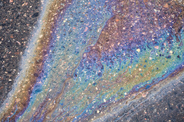 Gasoline spill on dark wet pavement displaying colorful iridescent film and abstract fluid patterns, symbolizing environmental impact