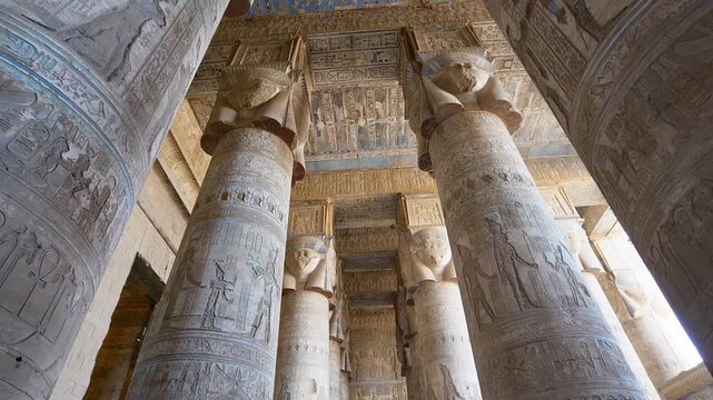 Dendera temple or Temple of Hathor. Painted columns with goddess faces and hieroglyphic ceiling of the hypostyle hall, ancient architecture with detailed carvings and blue painted zodiac. Egypt.