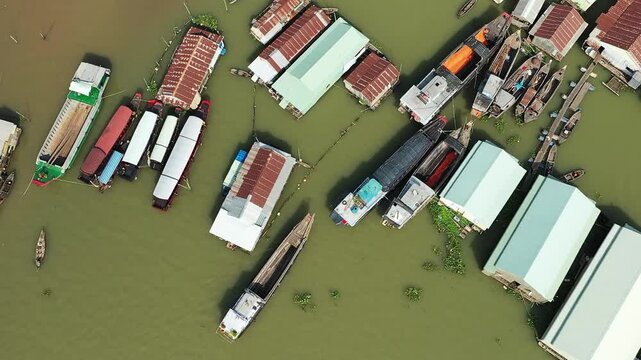 Aerial view of floating houses and boats on the river in Chau Doc, Vietnam, showcasing a unique riverside community. Traditional wooden boats and stilted structures are visible on the murky water.