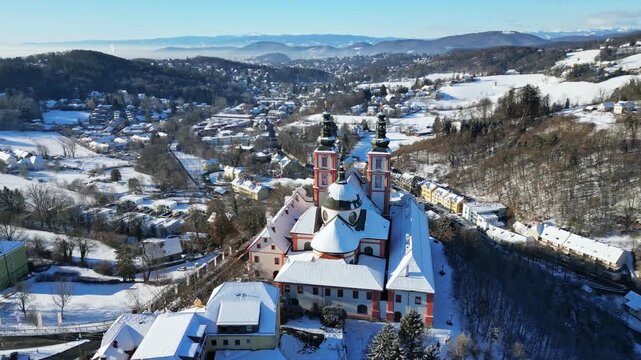 Aerial view of the historic Basilica Mariatrost with snowy roofs and white fields, contrasting with the clear blue sky, Graz, Styria, Austria.