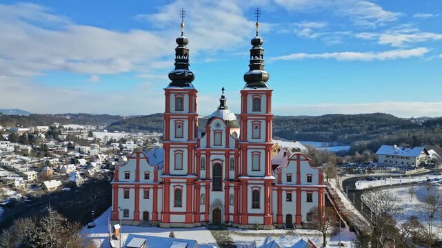 Aerial view of the red and white Basilica Mariatrost stands majestically against a backdrop of snowy fields and a blue sky, Graz, Styria, Austria.