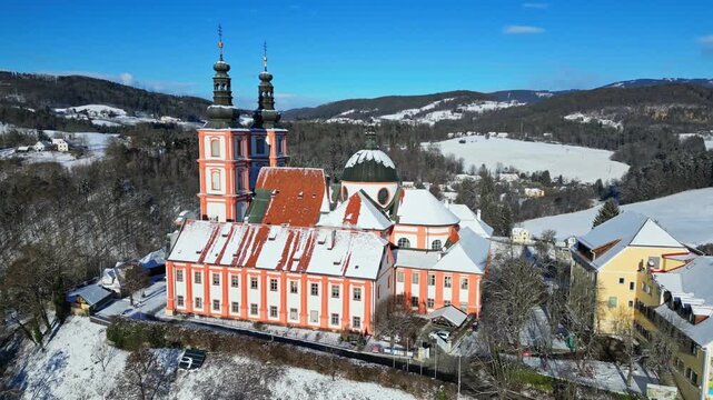 Aerial view of the Basilica Mariatrost, a majestic structure with snow-covered roofs, contrasting against the lush green landscape, Graz, Styria, Austria.