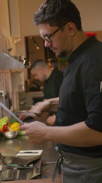 Professional chef sharpening kitchen knife with honing steel while preparing cooking tools for workday in restaurant kitchen. Vertical format footage