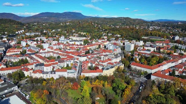 Aerial view of the city showcasing buildings with red roofs nestled amidst lush greenery and distant mountains, Graz, Styria, Austria.