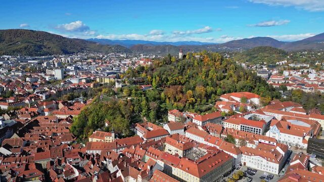 Aerial view of the city with red rooftops, Schlossberg hill and Uhrturm tower, a scenic blend of urban architecture and nature, Graz, Styria, Austria.