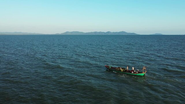 A traditional fishing boat sails across the calm blue waters near Kampot, Cambodia, with distant mountains on the horizon under a clear sky.