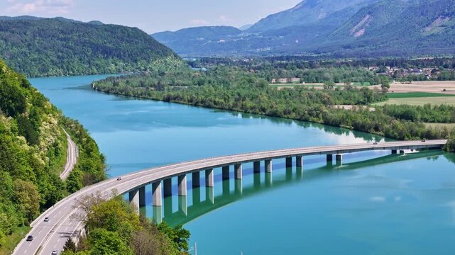 Aerial view of the River Drau flowing through lush green landscape and under a bridge, showcasing a blend of natural beauty and infrastructure, Ferlach, Carinthia, Austria.