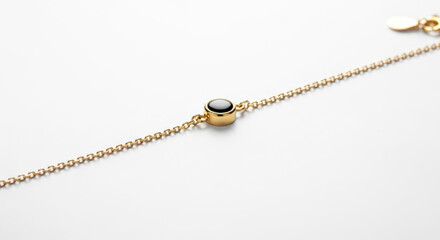 Fototapeta premium Close-up of a gold chain necklace with a black gemstone on a white background.