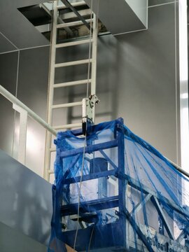 A blue ladder is suspended from a building. The ladder is attached to a blue tarp