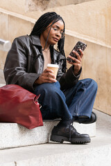 Fototapeta premium Young student using smartphone and drinking coffee on university steps