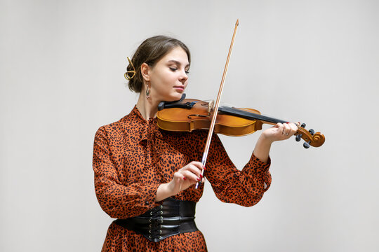young girl dressed in a brown dress stands on the stage and plays the violin.
