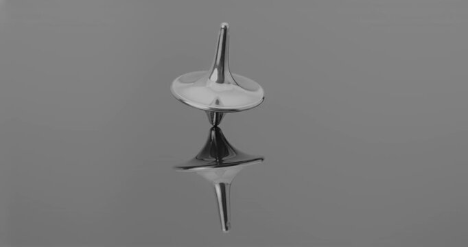 Metallic totem in initial steady rotation, gradually increasing wobble and tilt toward collapse against a mirrored backdrop.