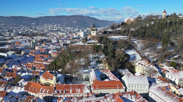 Aerial view of the Grazer Uhrturm clock tower perched atop a hill amidst the snowy rooftops and buildings, Graz, Styria, Austria.