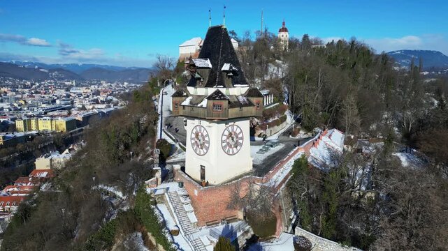 Aerial view of the Grazer Uhrturm, standing tall amidst the winter landscape, with snow-dusted trees and buildings, Graz, Styria, Austria.
