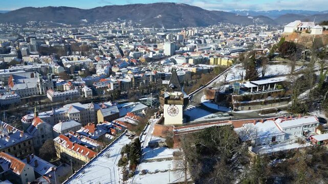 Aerial view of the snow-dusted Graz cityscape, featuring the iconic clock tower and the distant mountains, Graz, Styria, Austria.