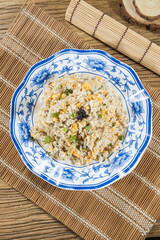 A blue porcelain bowl holds egg fried rice dotted with peas and scallion. Shot overhead on bamboo mats, the dish looks fluffy, simple and comforting for everyday meals.