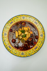 A decorative bowl holds tender fish slices submerged in a deep red chili oil broth with peppercorn, dried chiles and herbs. The top view highlights bold color and the signature heat of the dish.