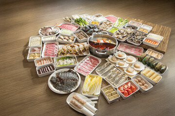 A wide table is filled with a grand hot pot spread. A dual broth pot sits in the center, surrounded by sliced meats, seafood, dumplings, vegetables, tofu, and noodles neatly arranged in trays and plat