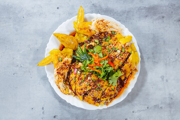 Chopped poached chicken is dressed in a glossy chili oil sauce with sesame, scallion and herbs. Served on a white plate, the overhead view shows heat, aroma and generous toppings.