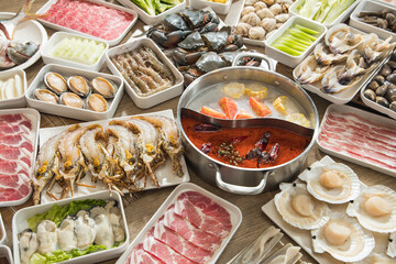 A generous hot pot setup features a dual broth pot surrounded by seafood, thin meats, dumplings, tofu and greens in orderly trays. The bright spread suggests a social meal ready for simmering.