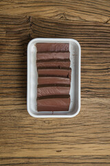 A white plastic tray holds neat slices of dark pork blood curd on a rustic wood surface. The simple overhead composition emphasizes a classic offal ingredient ready for hot pot or stir fry.