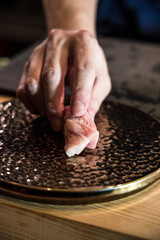 At a sushi counter, a chef places a piece of nigiri on a hammered metal plate. The close focus reveals rice grain texture and the sheen of fresh fish for an artisan service moment.