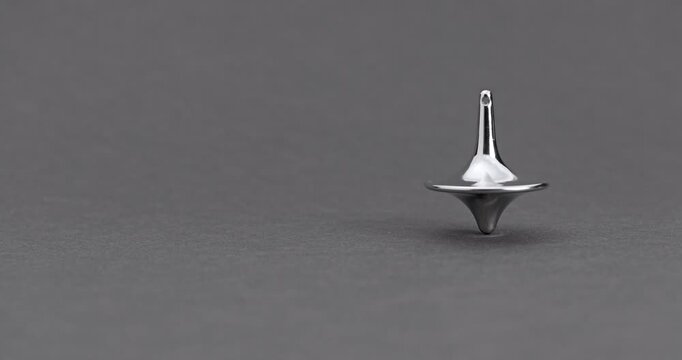 Metallic Spinning Top Falling Over. Linear footage of a shiny chrome top in steady rotation, progressively wobbling with increasing tilt until it fully topples on a matte gray surface.
