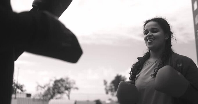 Curvy african girl and her personal trainer doing boxing exercise outdoor - Sport, motivation, diet and healthy lifestyle concept - Black and white editing
